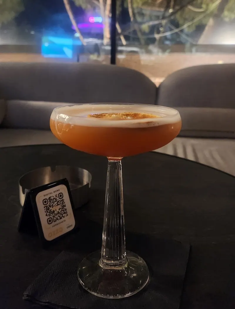 An orange sour cocktail with a foam top in a coupe glass