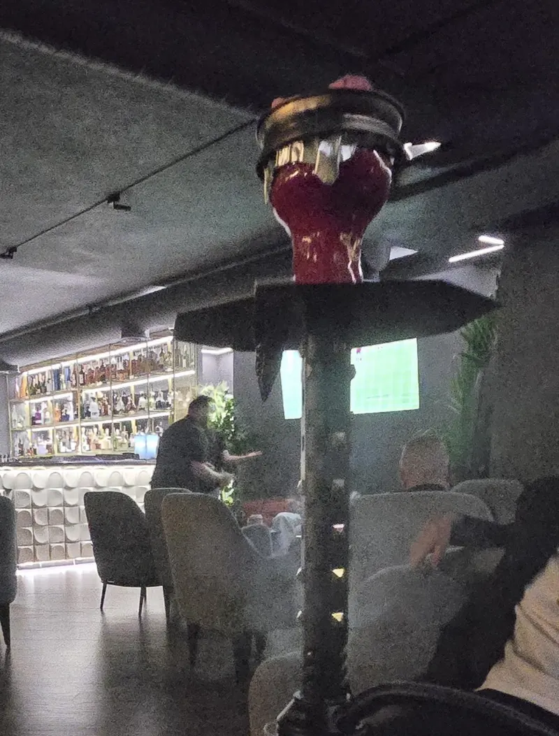 A shisha with a red bowl in the lounge, the bar lit up behind it