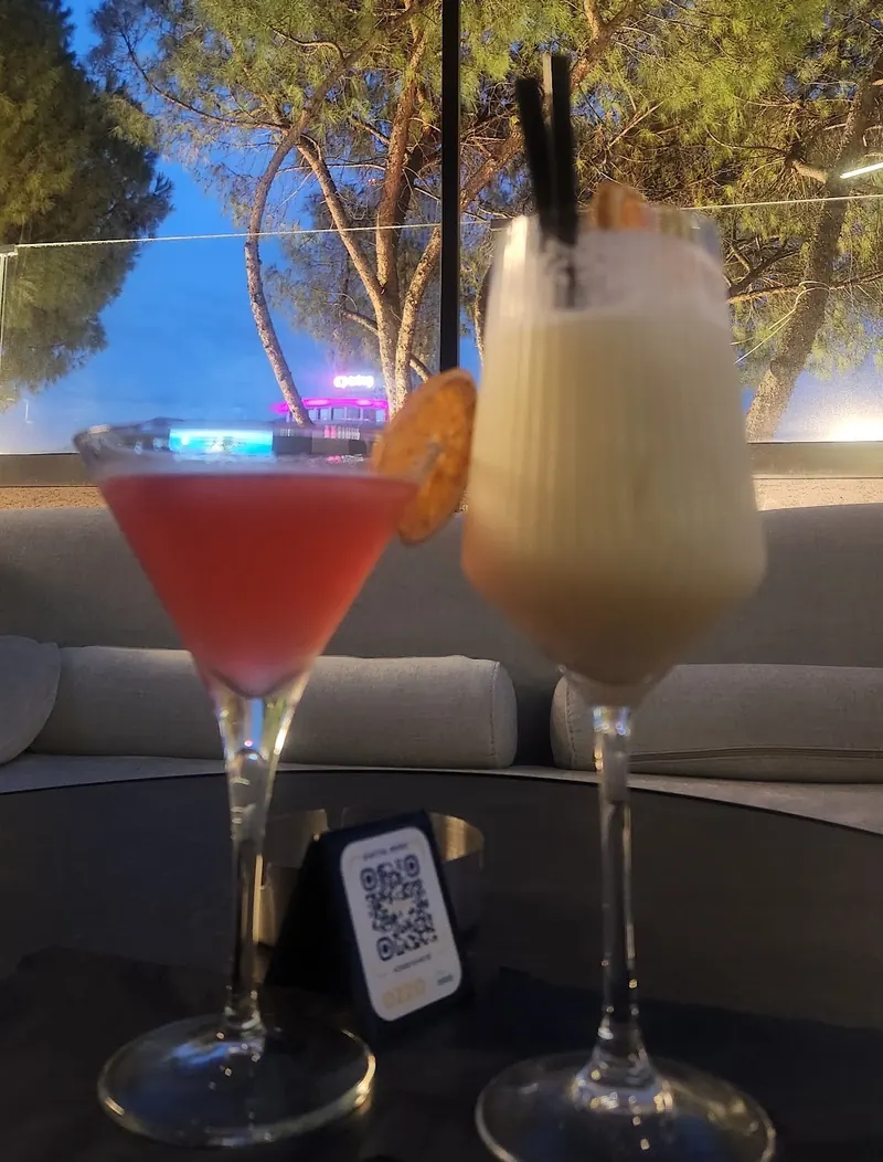 A pink cocktail and a creamy cocktail on the terrace at dusk, pines behind