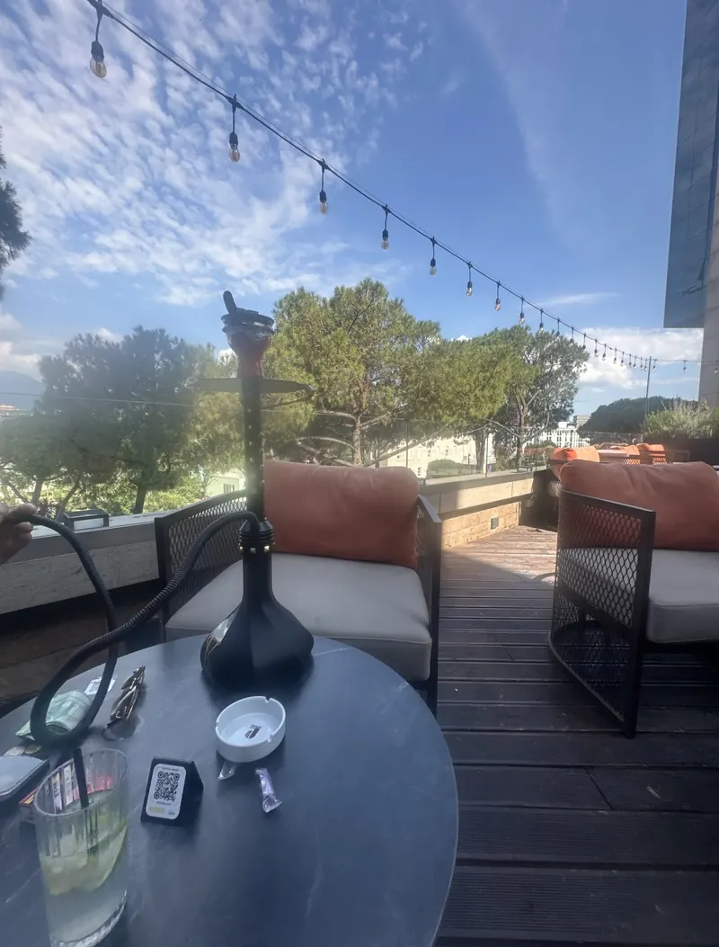 A shisha on a terrace table under a blue sky, orange cushions on the sofas