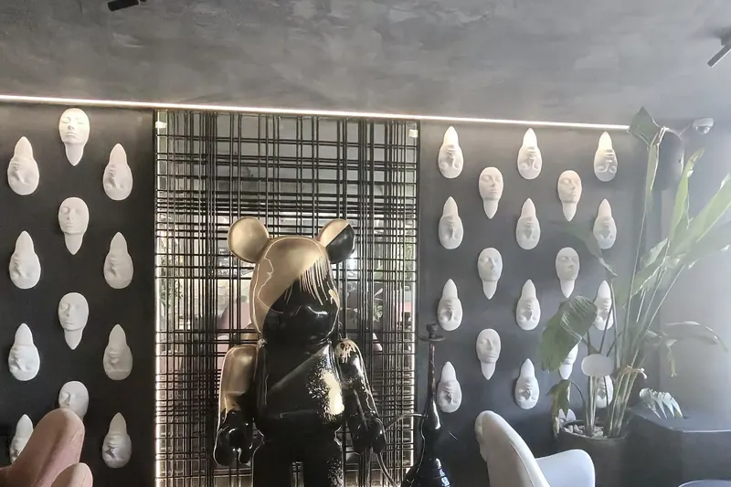 The lounge interior: a wall of white masks, the bear sculpture and pink armchairs